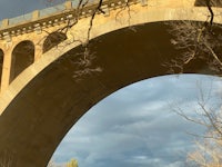 a bridge with arches over a river under a cloudy sky