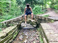 a man sitting on a stone bridge in the woods