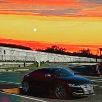 a black audi parked in a parking lot at sunset