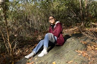 a woman sitting on a rock in the woods