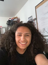 a man with curly hair smiling in front of a desk