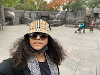 a woman wearing a hat and sunglasses in front of a waterfall