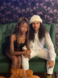 two women sitting on a green couch with skulls on the wall