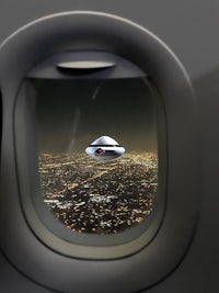 an airplane window with a ufo flying over a city